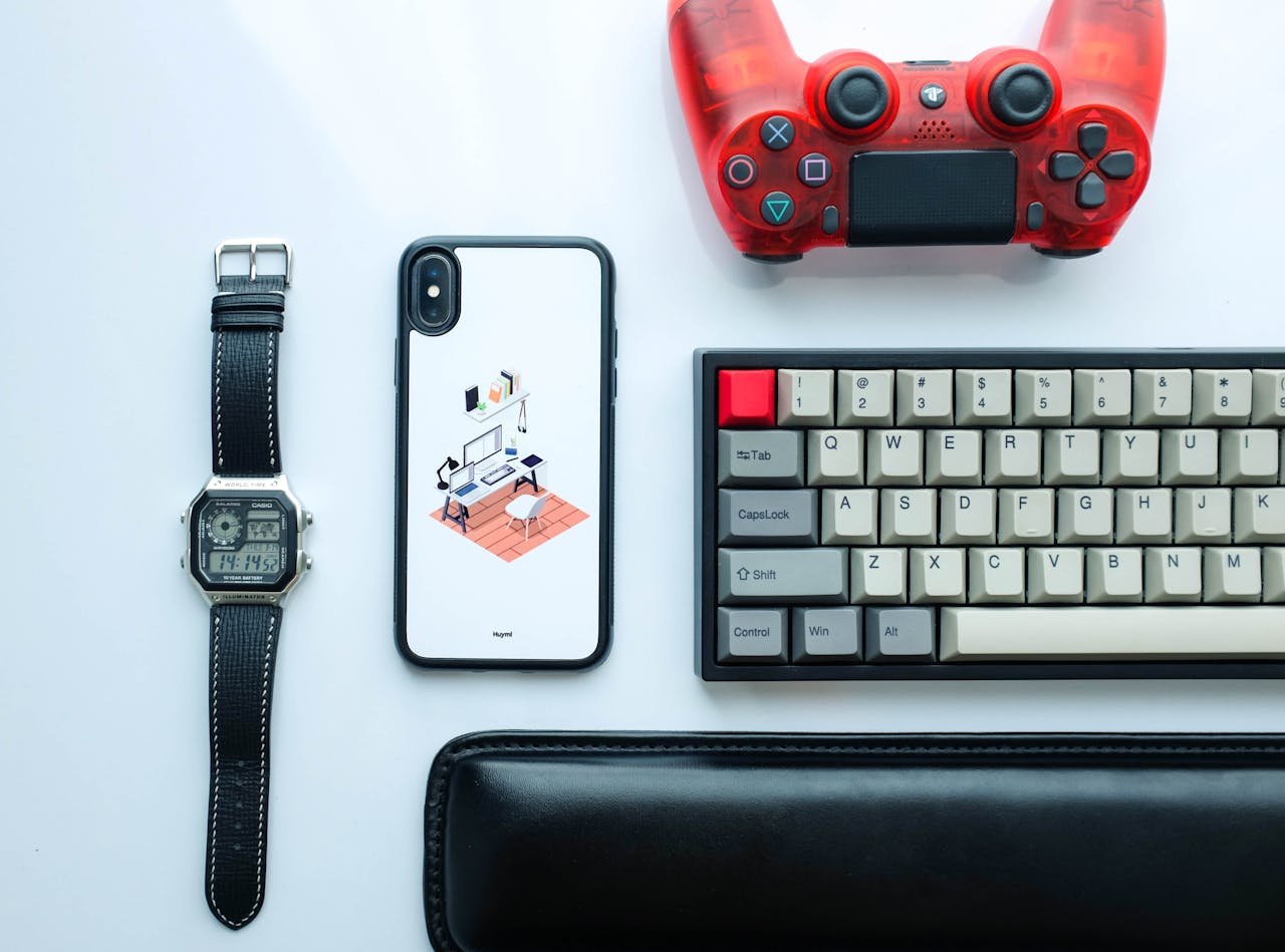 Top view of modern gadgets including a smartphone, watch, game controller, and keyboard.
