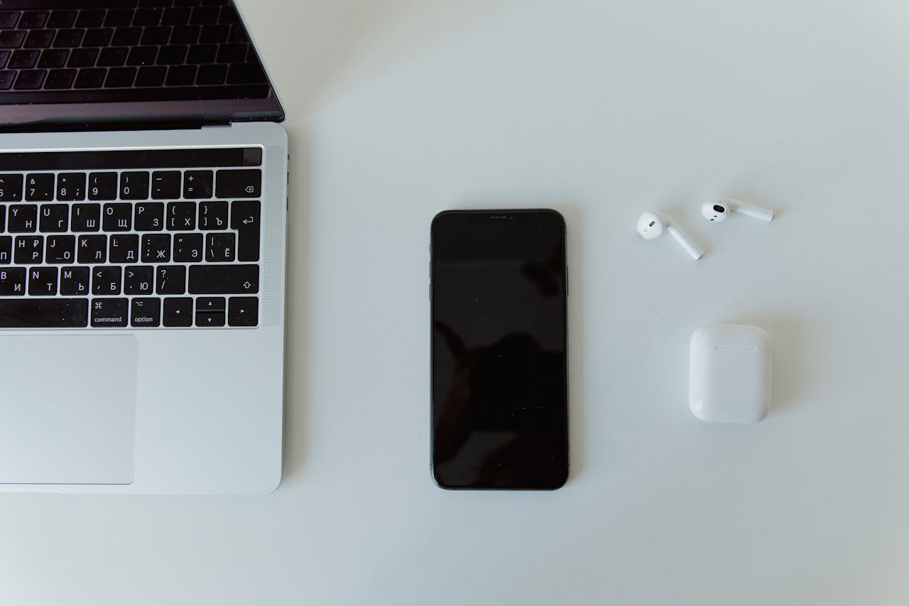 team-03 Top view of a laptop, smartphone, and wireless earphones on a white desk.